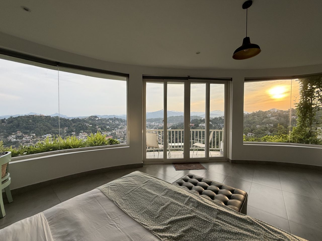 Guest bedroom with curved corner windows framing a sunset over the Kandy hills at The Summit Kandy